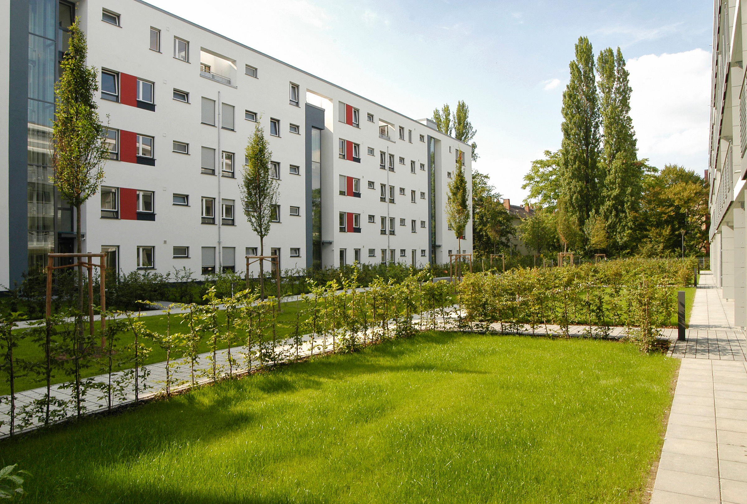 Großer moderner Wohngebäudekomplex mit frisch angelegter, gepflegter Grünflächer und junger Bäume davor