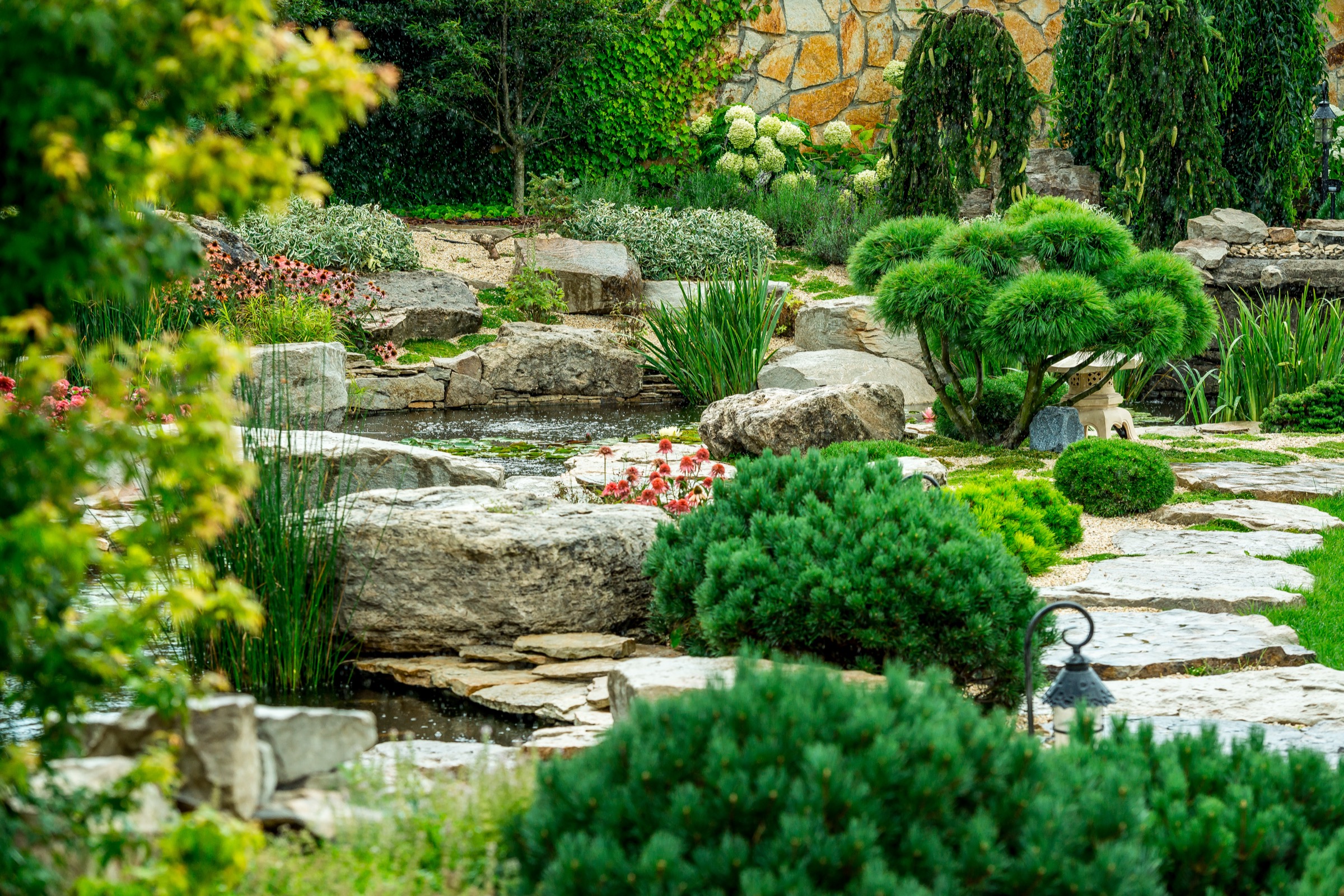 Ein Teilausschnitt eines Gartens mit kleinem Bachlauf durch Steine und verschiedene Grünpflanzen.